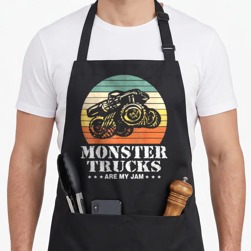 Engine truck apron - Retro monster truck in striped circle with white text MONSTER TRUCKS ARE MY JAM — shown on a black cotton canvas apron against a white background