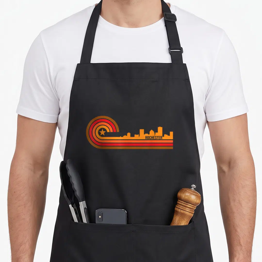 Cityscape rochester apron - Retro Rochester skyline with brown red orange yellow stripes and star on left — shown on a black cotton canvas apron against a white background
