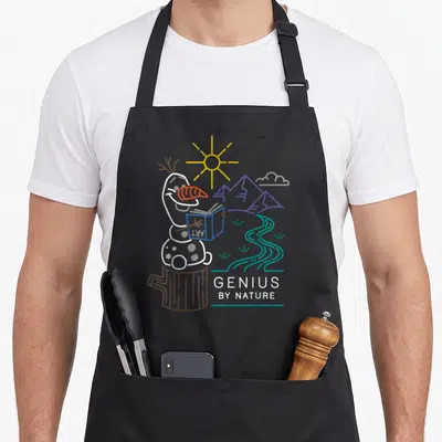 Genius frozen apron - Snowman reading book on stump with GENIUS BY NATURE text and landscape — shown on a black cotton canvas apron against a white background