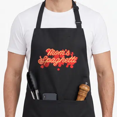 Spaghetti mother's day aprons - Stacked Mom's Spaghetti text in red and yellow over sauce splatters — shown on a black cotton canvas apron against a white background