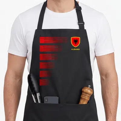 Albania pride apron - Minimalist graphic with six red line stacks, yellow ALBANIA text, and coat of arms shield — shown on a black cotton canvas apron against a white background