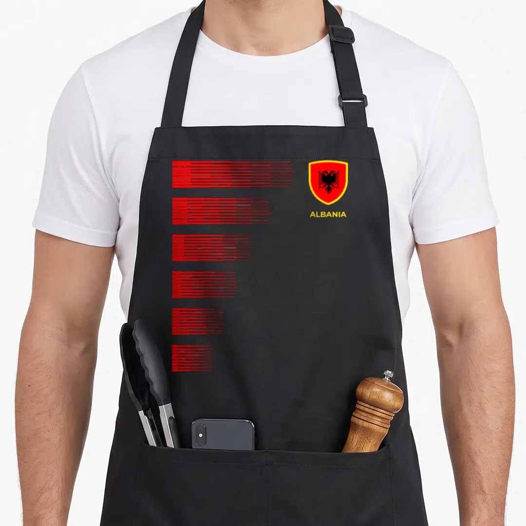 Albania pride apron - Minimalist graphic with six red line stacks, yellow ALBANIA text, and coat of arms shield — shown on a black cotton canvas apron against a white background