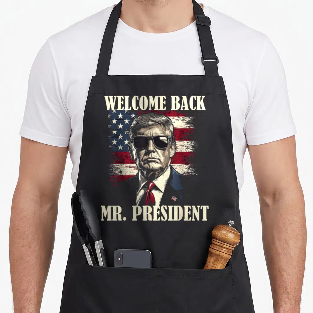 Welcome mr apron - Donald Trump portrait with distressed flag and Welcome Back Mr President text — shown on a black cotton canvas apron against a white background