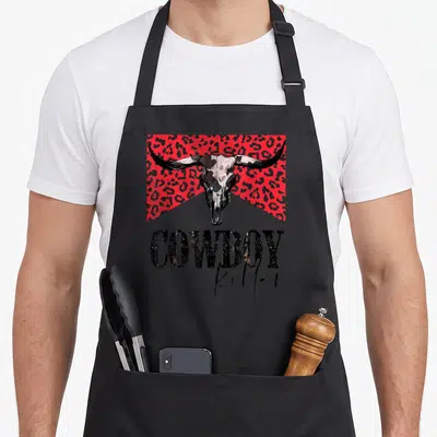 Leopard western apron - Distressed bull skull on red leopard rectangle above stacked cowboy killer text — shown on a black cotton canvas apron against a white background