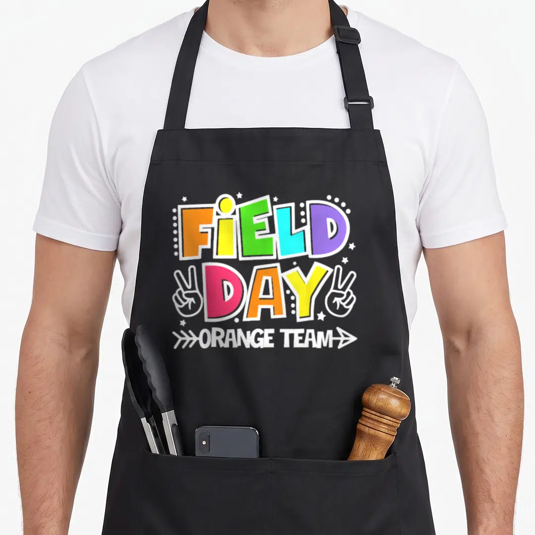 Field game teacher apron - Colorful stacked FIELD DAY ORANGE TEAM text with peace sign hands and stars in orange yellow — shown on a black cotton canvas apron against a white background