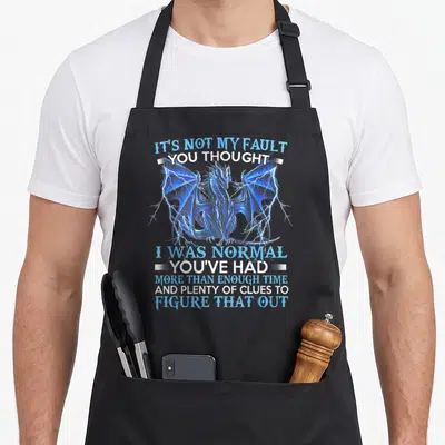 Fault dragon apron - Blue dragon with lightning and sarcastic text about being normal — shown on a black cotton canvas apron against a white background