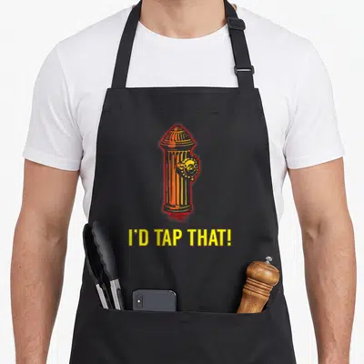 Tap firefighter apron - Orange fire hydrant cartoon above yellow I'D TAP THAT text — shown on a black cotton canvas apron against a white background