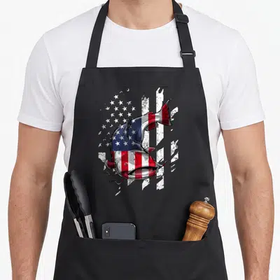 Catfishing fisherman apron - Cartoon catfish filled with US flag pattern on distressed background — shown on a black cotton canvas apron against a white background