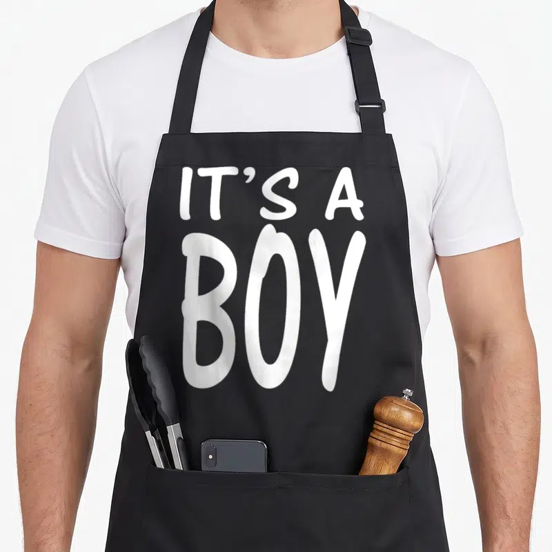 Blue baby shower apron - White IT'S A BOY stacked typography on black fabric — shown on a black cotton canvas apron against a white background