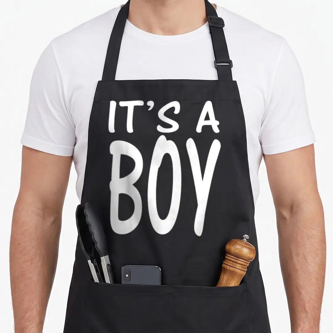 Blue baby shower apron - White IT'S A BOY stacked typography on black fabric — shown on a black cotton canvas apron against a white background