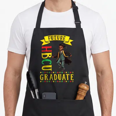 Future best college ever apron - Cartoon boy in graduation cap gown with FUTURE HBCU GRADUATE text and colorful diamonds — shown on a black cotton canvas apron against a white background