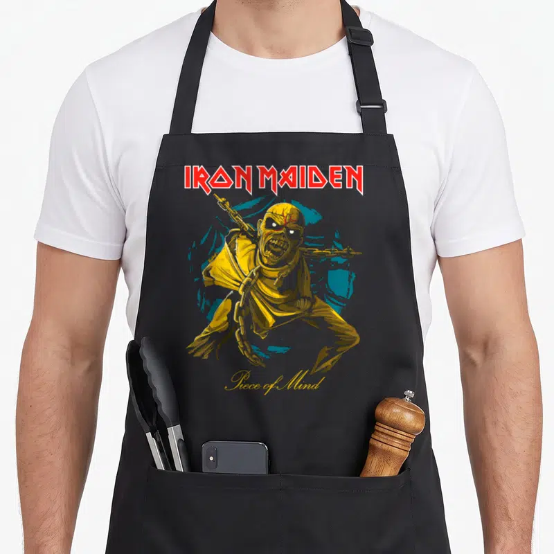 Pom camping apron - Cartoon mummy with chains in yellow and red in front of a blue circle under Iron Maiden text — shown on a black cotton canvas apron against a white background