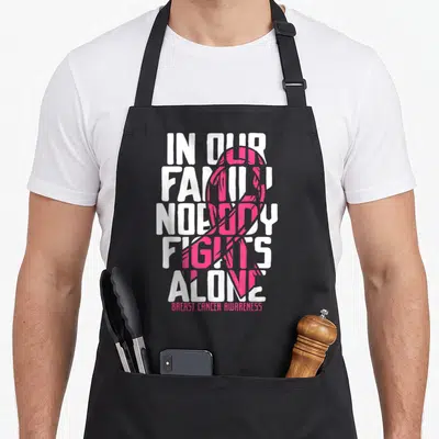 Funny support breast cancer awareness aprons - White stacked text In Our Family Nobody Fights Alone overlapped — shown on a black cotton canvas apron against a white background