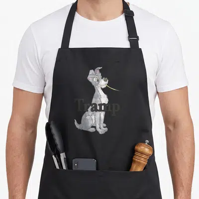 Funny spaghetti lady and the tramp apron - Grey cartoon dog holding yellow strand with Tramp text across body — shown on a black cotton canvas apron against a white background