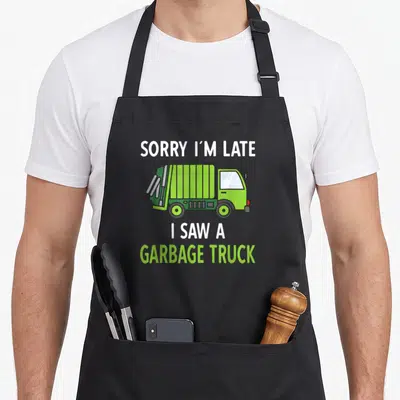 Saw truck apron - Cartoon lime green garbage truck with text SORRY I'M LATE I SAW A GARBAGE TRUCK — shown on a black cotton canvas apron against a white background