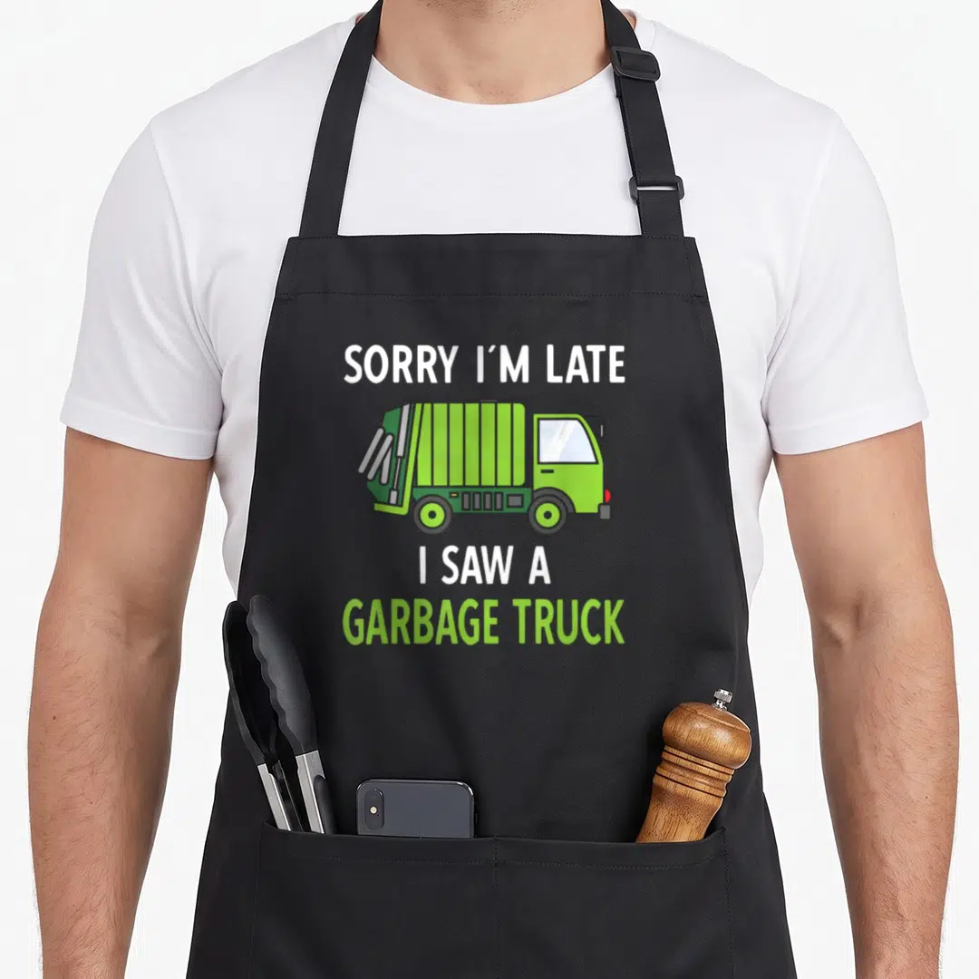 Saw truck apron - Cartoon lime green garbage truck with text SORRY I'M LATE I SAW A GARBAGE TRUCK — shown on a black cotton canvas apron against a white background