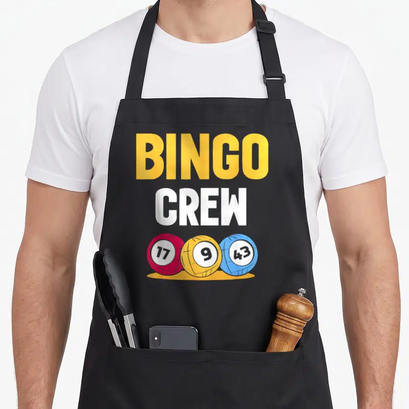 Game bingo apron - BINGO CREW text above red yellow blue numbered balls — shown on a black cotton canvas apron against a white background