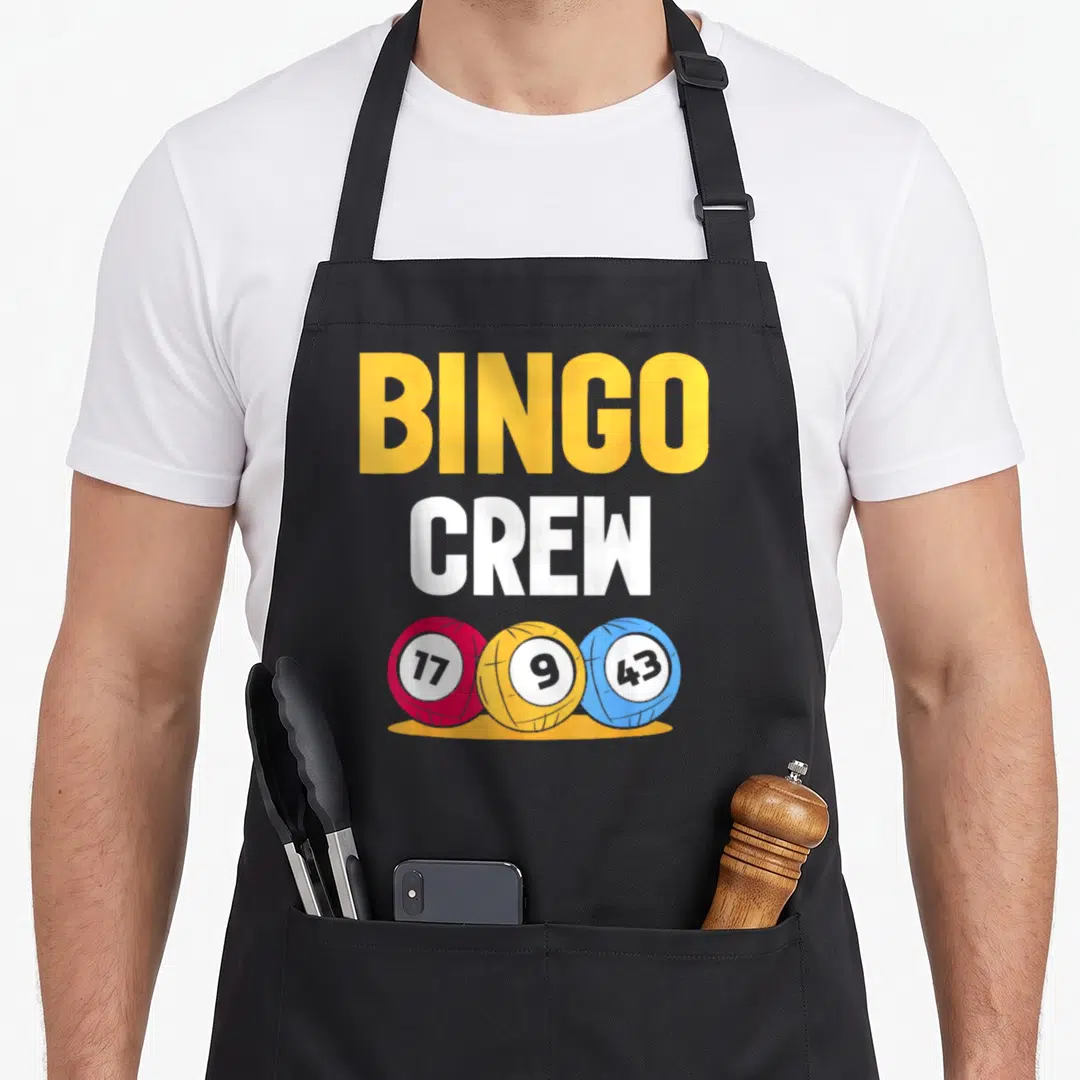 Game bingo apron - BINGO CREW text above red yellow blue numbered balls — shown on a black cotton canvas apron against a white background