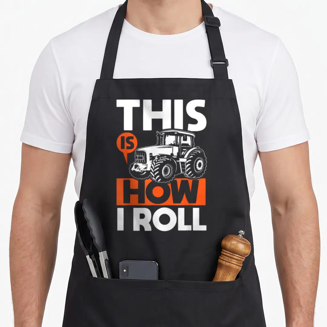 Roll farming apron - Tractor graphic with THIS IS HOW I ROLL text in white and orange — shown on a black cotton canvas apron against a white background