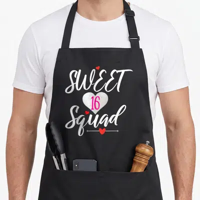 Sixteen youth birthday apron - SWEET 16 Squad text with silver glitter heart and small red hearts on white script — shown on a black cotton canvas apron against a white background