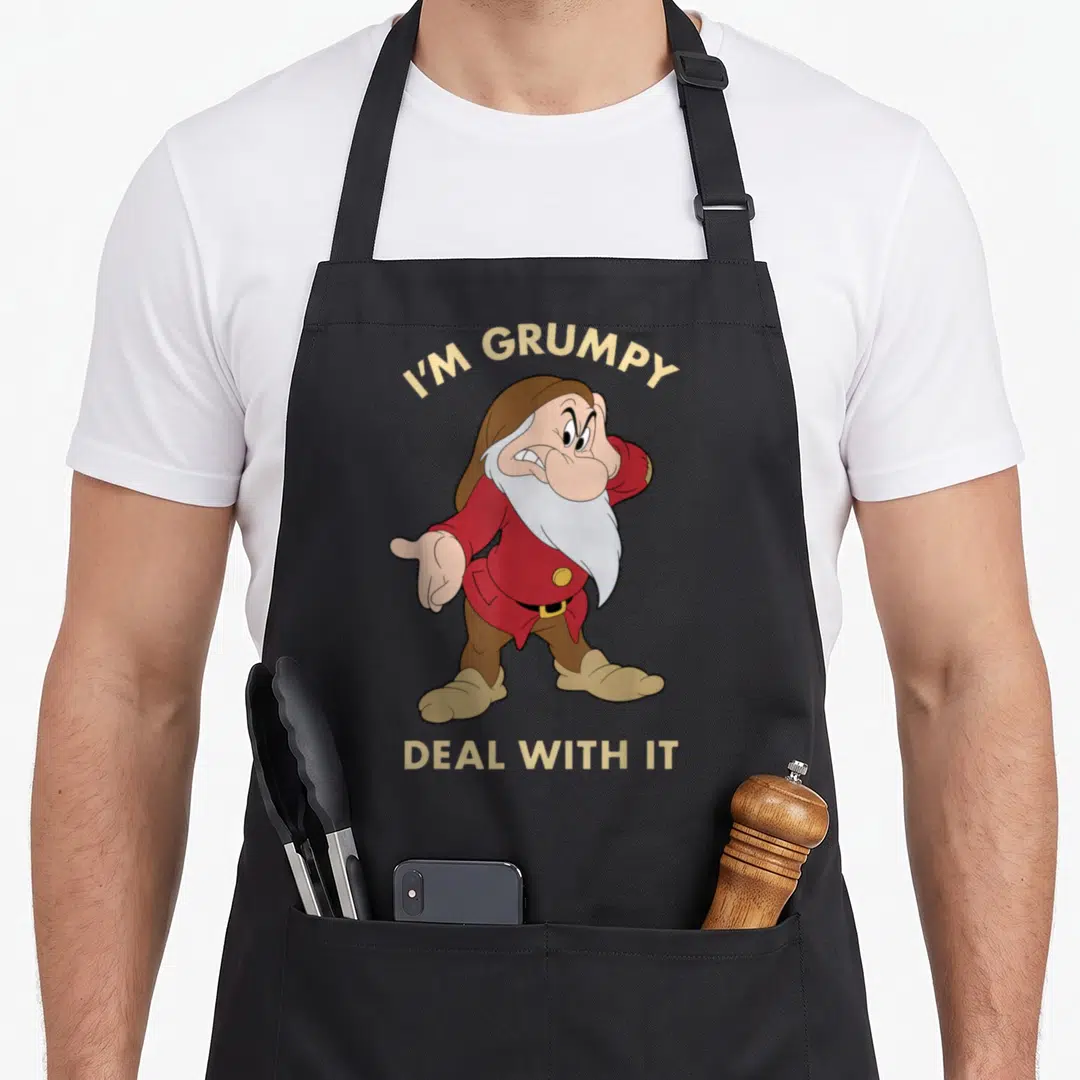 Grumpy snow white apron - Cartoon dwarf in red shirt with I'M GRUMPY DEAL WITH IT text in tan and white — shown on a black cotton canvas apron against a white background