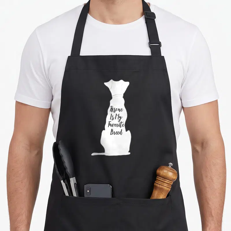 Owner top dog aprons - White sitting dog silhouette with grey text Rescue Is My Favorite Breed inside — shown on a black cotton canvas apron against a white background