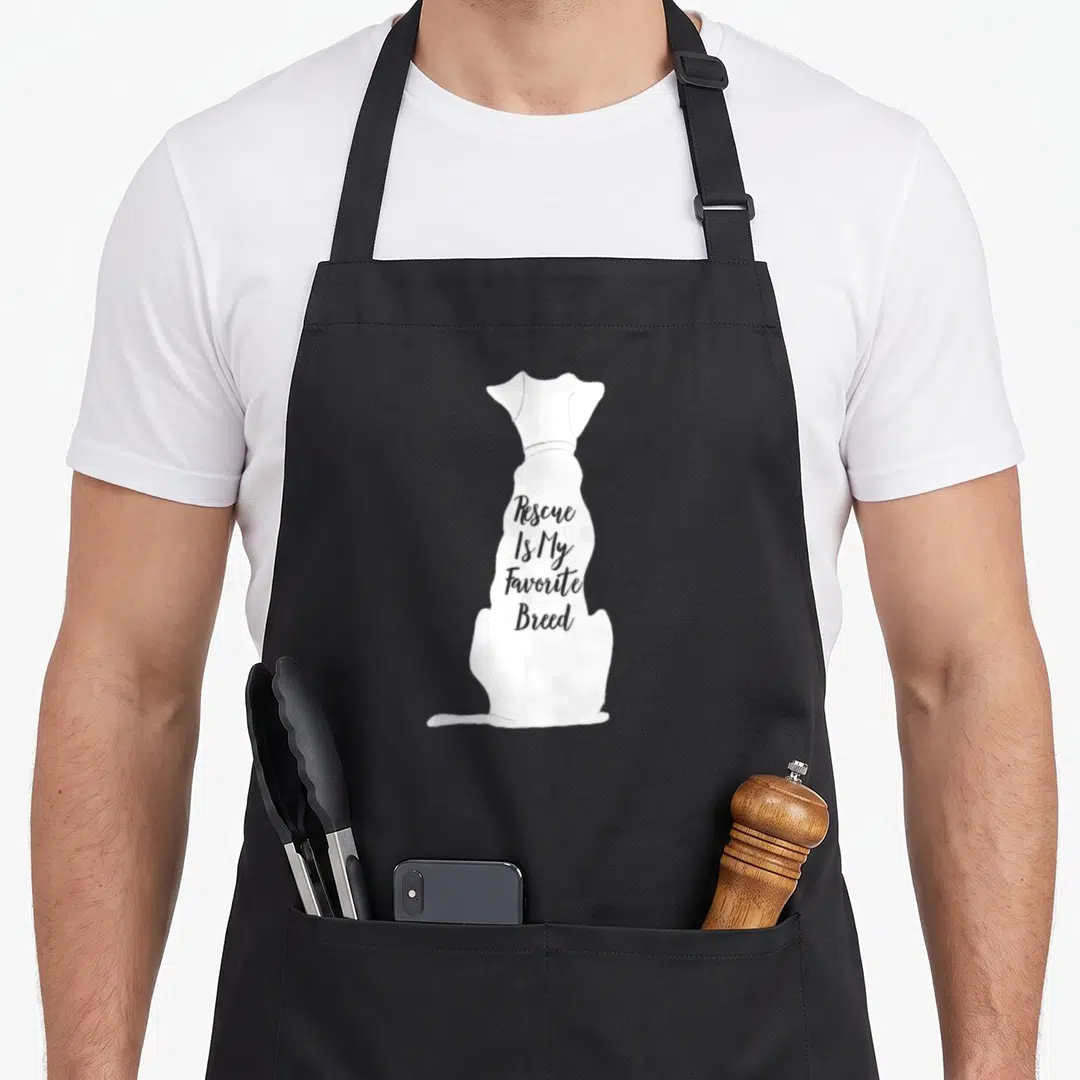 Owner top dog aprons - White sitting dog silhouette with grey text Rescue Is My Favorite Breed inside — shown on a black cotton canvas apron against a white background