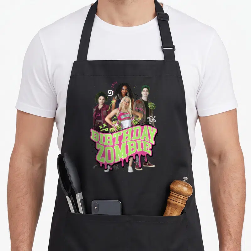 Zomby birthday apron - BIRTHDAY ZOMBIE text in lime green and pink dripping over four people with brain and skull — shown on a black cotton canvas apron against a white background