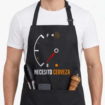 Beer mexican apron - Minimalist fuel gauge with needle at E, beer mug at F, necesito cerveza text in white and orange — shown on a black cotton canvas apron against a white background