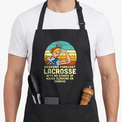 Strong mama apron - Retro woman flexing with crossed lacrosse sticks and forecast text on striped background — shown on a black cotton canvas apron against a white background