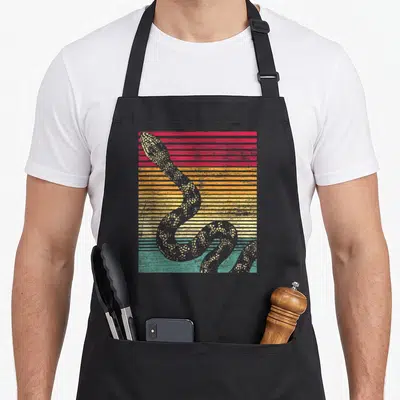 Funny snake lover apron - Grey coiled snake over retro red orange yellow and teal horizontal stripes — shown on a black cotton canvas apron against a white background