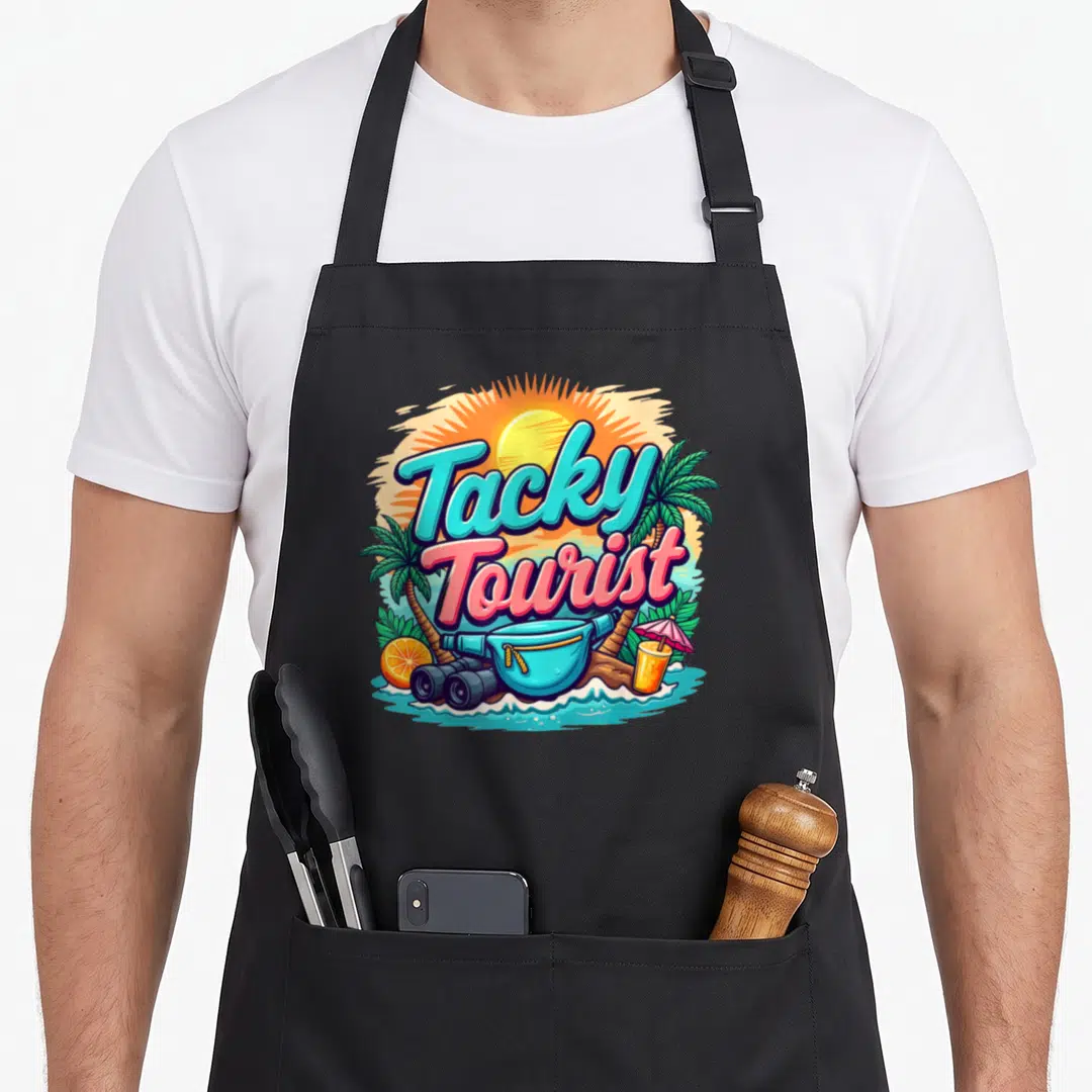 Vacay chef outfit with apron - Tacky Tourist text with fanny pack, binoculars, drink, and palm trees in cyan pink — shown on a black cotton canvas apron against a white background