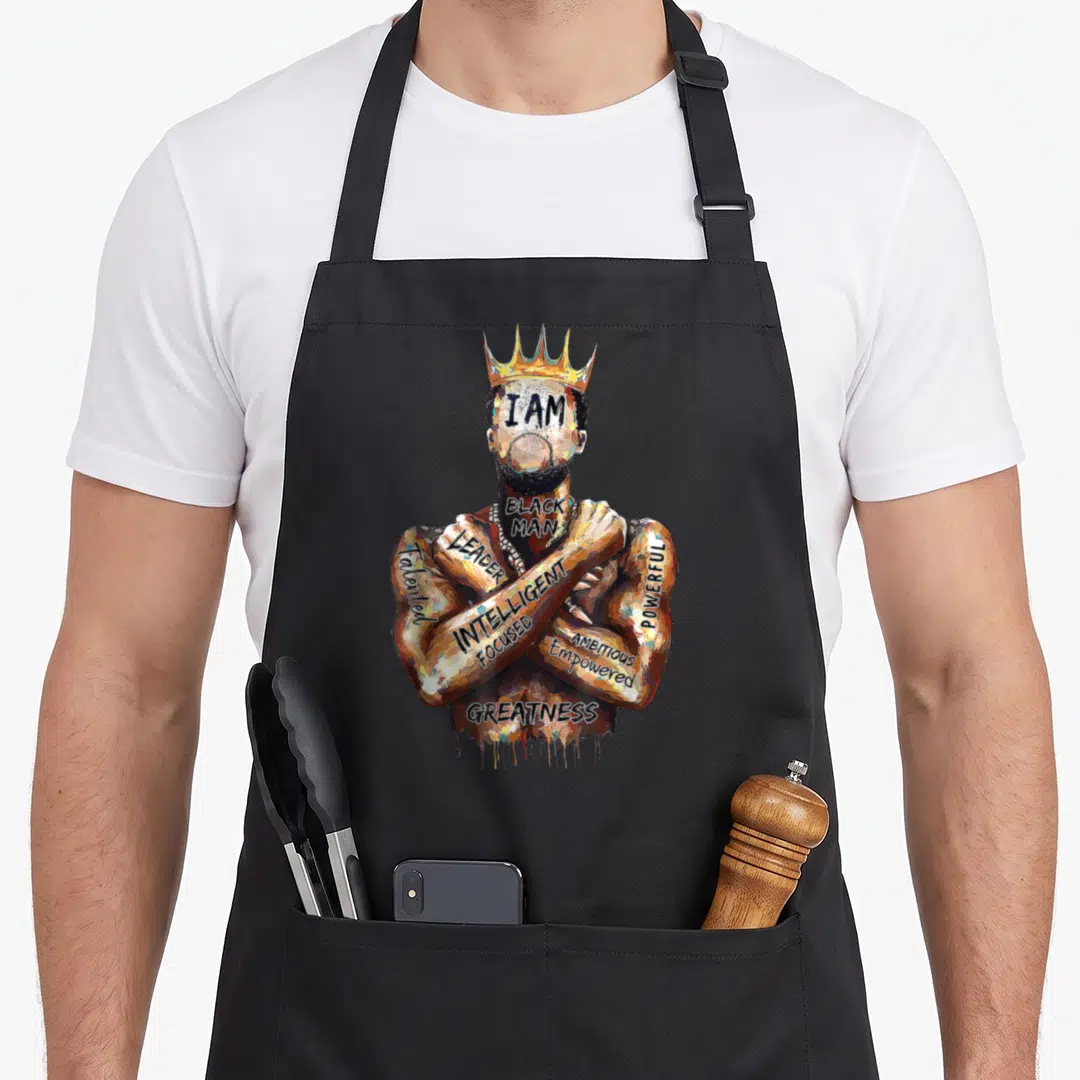 Afro king apron - Watercolor man with gold crown and text I AM BLACK MAN LEADER on crossed arms — shown on a black cotton canvas apron against a white background