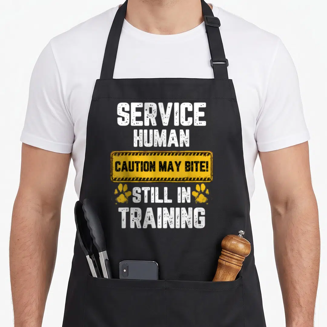 Caution dog training apron - Service Human Caution May Bite Still In Training sign with paw prints — shown on a black cotton canvas apron against a white background