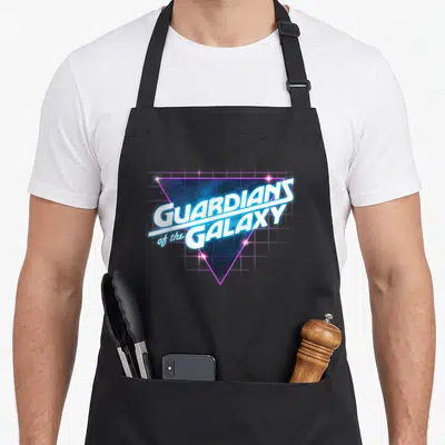 Guardian line apron - Stacked white Guardians of the Galaxy text over a glowing purple blue starry triangle grid — shown on a black cotton canvas apron against a white background