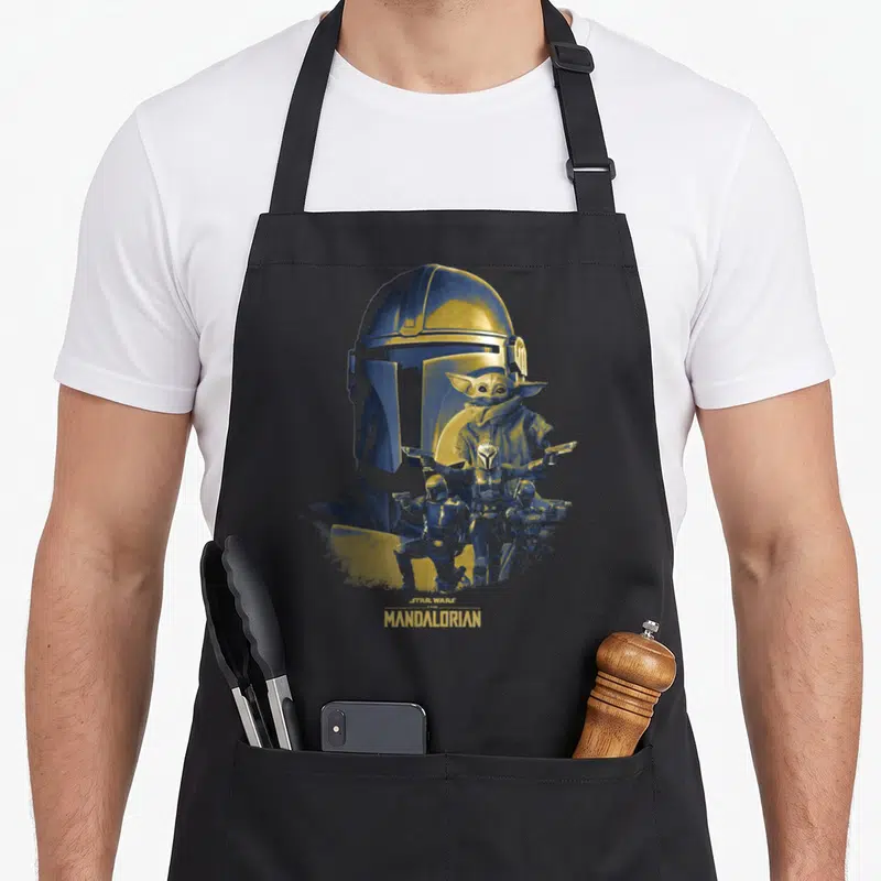 Shot neat apron - Mandalorian helmet Grogu three warriors blue yellow text Star Wars The Mandalorian — shown on a black cotton canvas apron against a white background