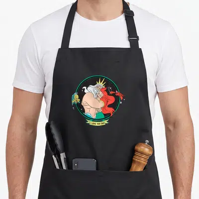 Triton father day apron - King Triton and Ariel hugging in teal circle with Flounder Sebastian and I LOVE YOU DAD banner — shown on a black cotton canvas apron against a white background