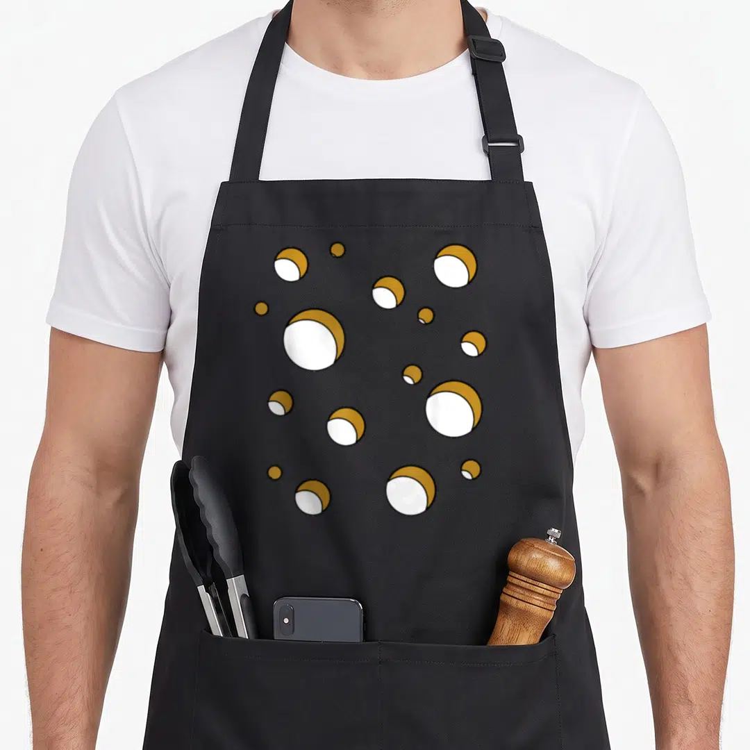 Cheese swiss apron - Scattered gold and white spherical shapes on black fabric — shown on a black cotton canvas apron against a white background