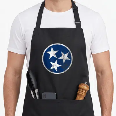 Tennessee traditional apron - Distressed blue circle containing three white five-pointed stars arranged in a triangular — shown on a black cotton canvas apron against a white background