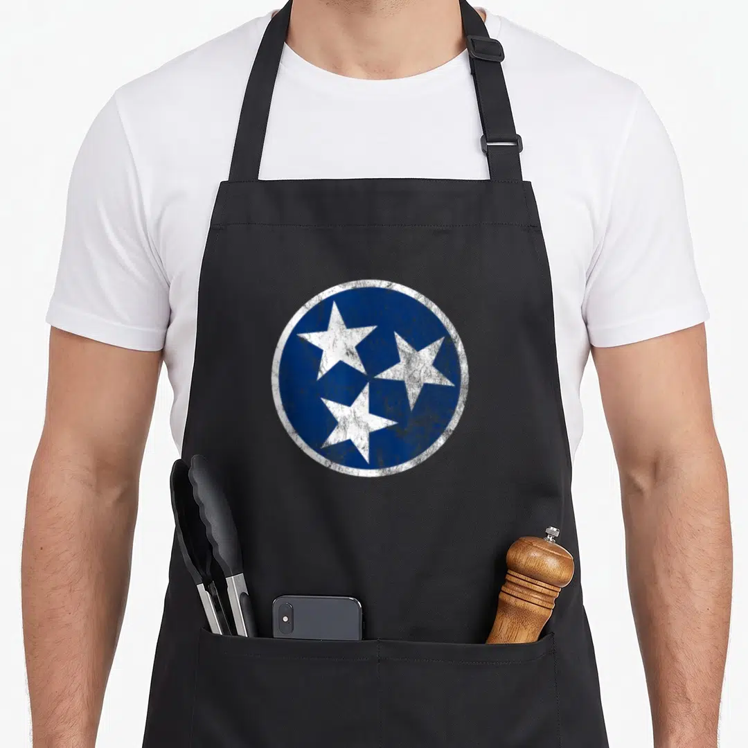 Tennessee traditional apron - Distressed blue circle containing three white five-pointed stars arranged in a triangular — shown on a black cotton canvas apron against a white background