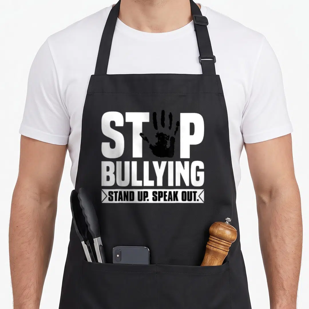 Stop unity day apron - White STOP BULLYING text with black handprint replacing O and STAND UP SPEAK OUT banner — shown on a black cotton canvas apron against a white background
