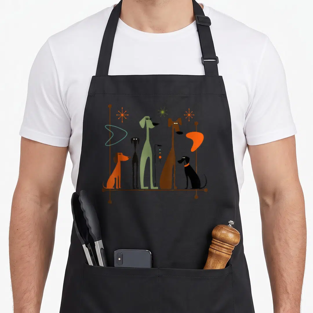 Dog modern apron - Five stylized dogs in orange, green, and brown standing on a line with retro atomic starburst shapes — shown on a black cotton canvas apron against a white background