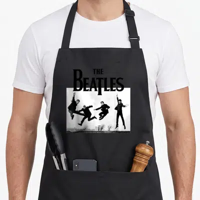 Jump red officially apron - THE BEATLES text above photo of four men jumping in black and white — shown on a black cotton canvas apron against a white background