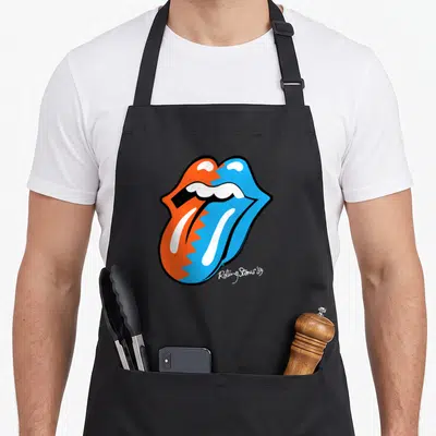 Zig rolling stones apron - Split orange and blue mouth with tongue out and white Rolling Stones '89 script text — shown on a black cotton canvas apron against a white background