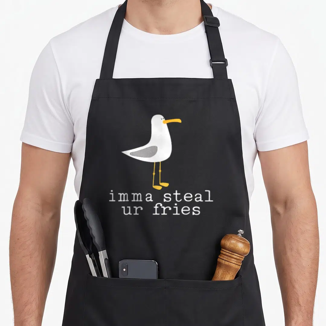 Imma bird apron - Cartoon seagull with orange beak above text imma steal ur fries in white — shown on a black cotton canvas apron against a white background