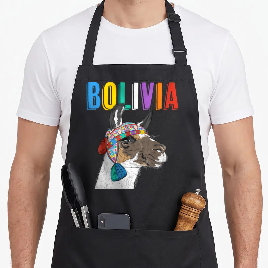 Bolivia alpaca apron - Cartoon llama with geometric headband under multicolored BOLIVIA text — shown on a black cotton canvas apron against a white background