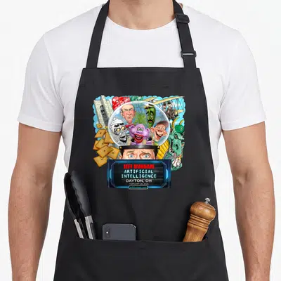Dunham dayton apron - Jeff Dunham cartoon eyes under glass dome with puppets crackers and blue text box — shown on a black cotton canvas apron against a white background