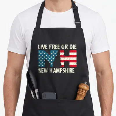 Hampshire patriotic apron - LIVE FREE OR DIE NH letters with US flag pattern and NEW HAMPSHIRE text in distressed white — shown on a black cotton canvas apron against a white background