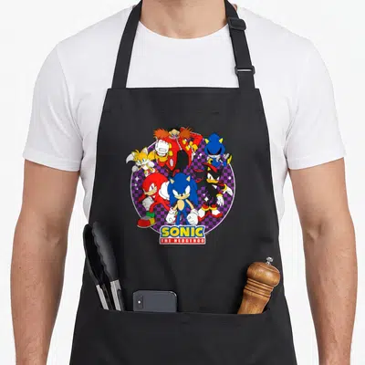 Heroe crazy hedgehog man apron - Sonic characters clustered over purple checkerboard circle with SONIC THE HEDGEHOG logo — shown on a black cotton canvas apron against a white background
