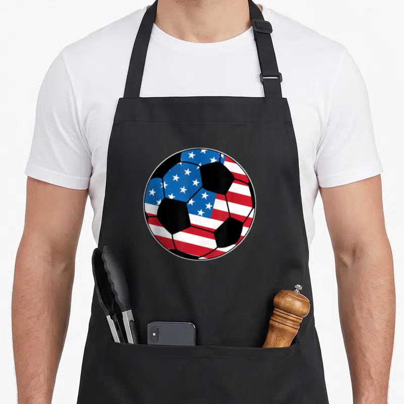 State stripe apron - Soccer ball with US flag pattern in red white blue and black — shown on a black cotton canvas apron against a white background